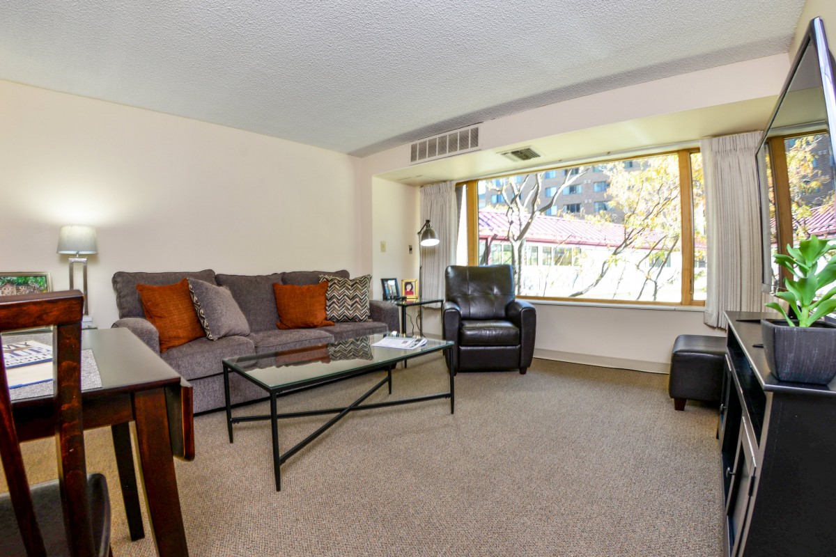 A cozy living room featuring a sofa, armchair, and coffee table with a large window providing natural light.
