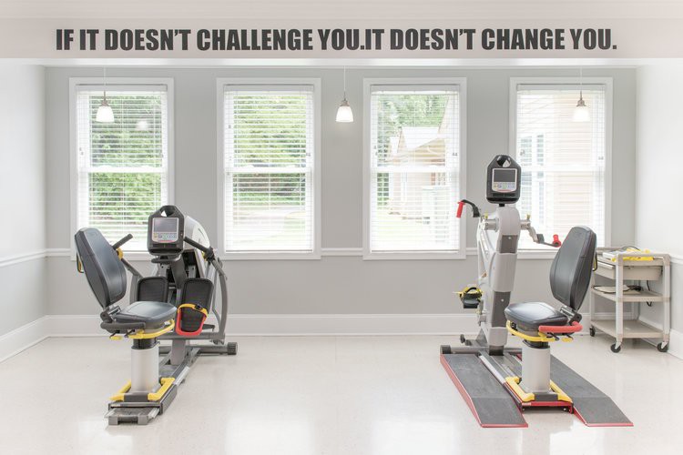 A bright gym space with exercise machines and a motivational quote on the wall.