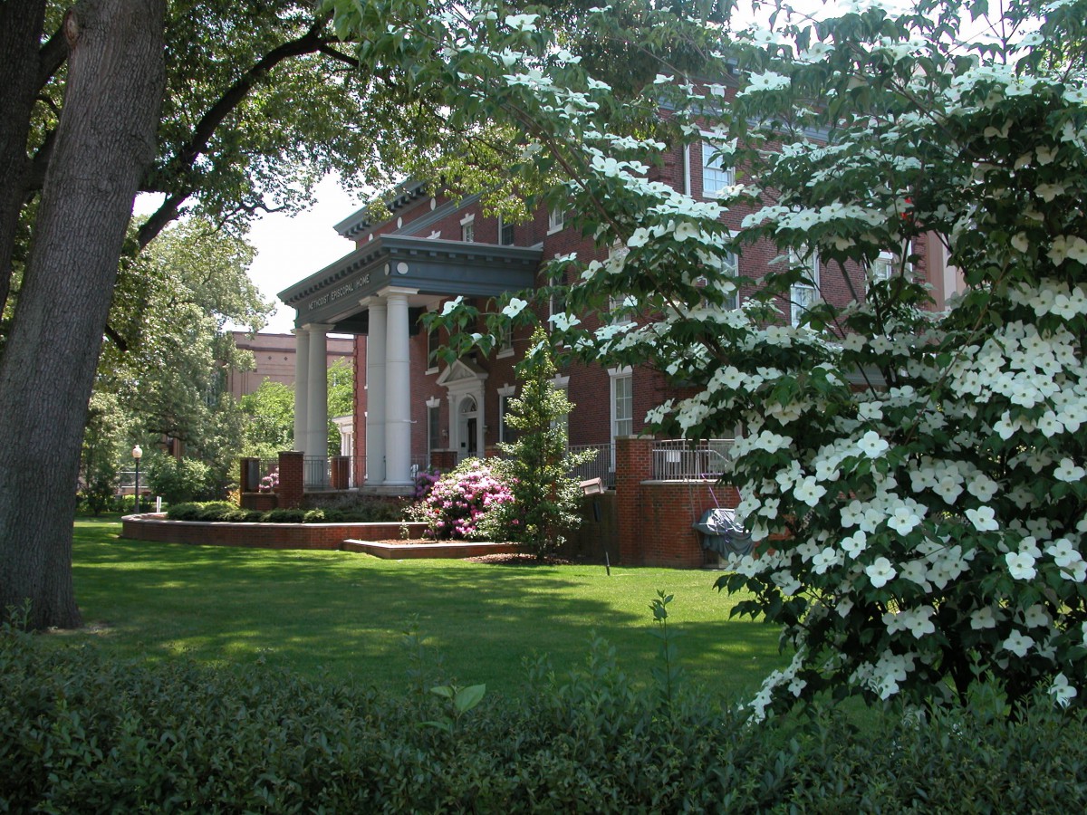 A beautiful brick house surrounded by a lush garden with blooming trees and flowers.