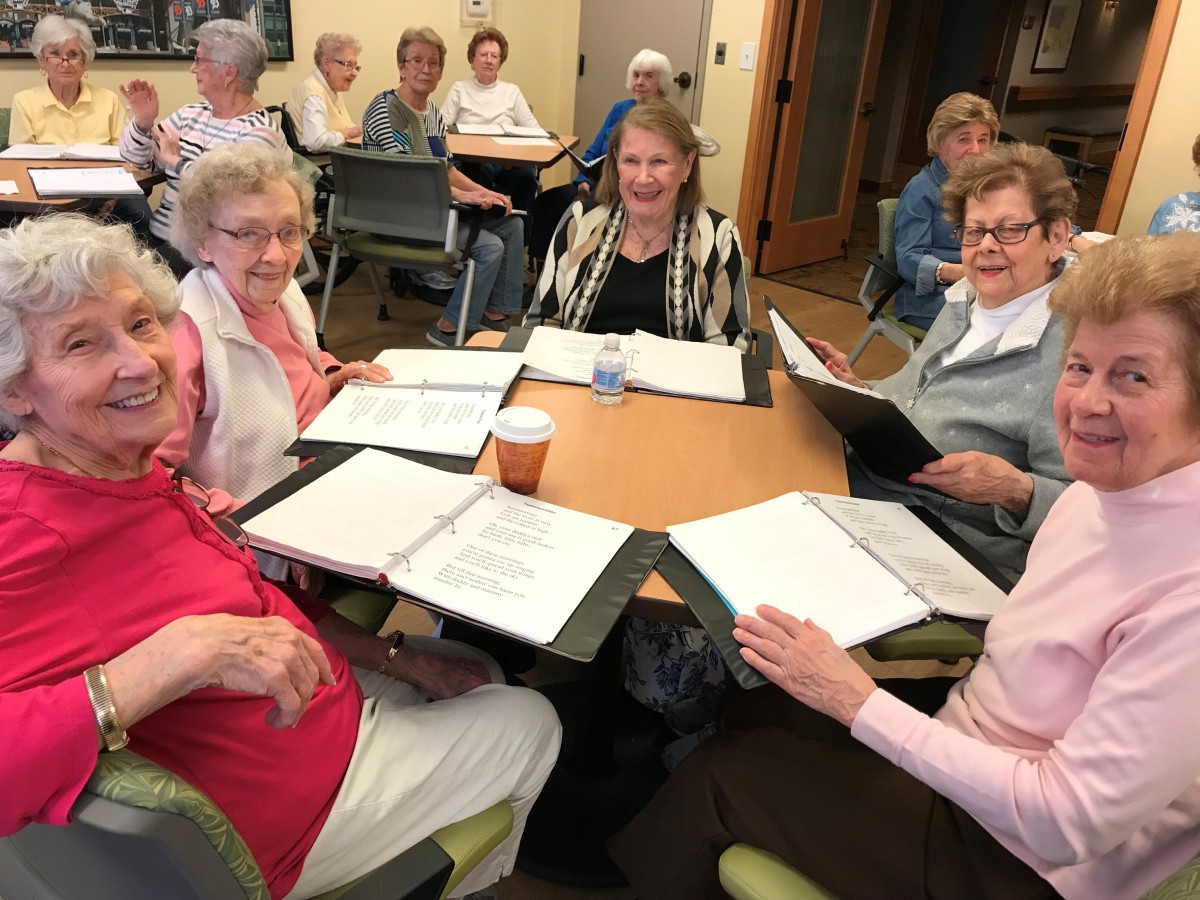 A group of seniors gathered around a table in a meeting, engaged in discussion and smiling.