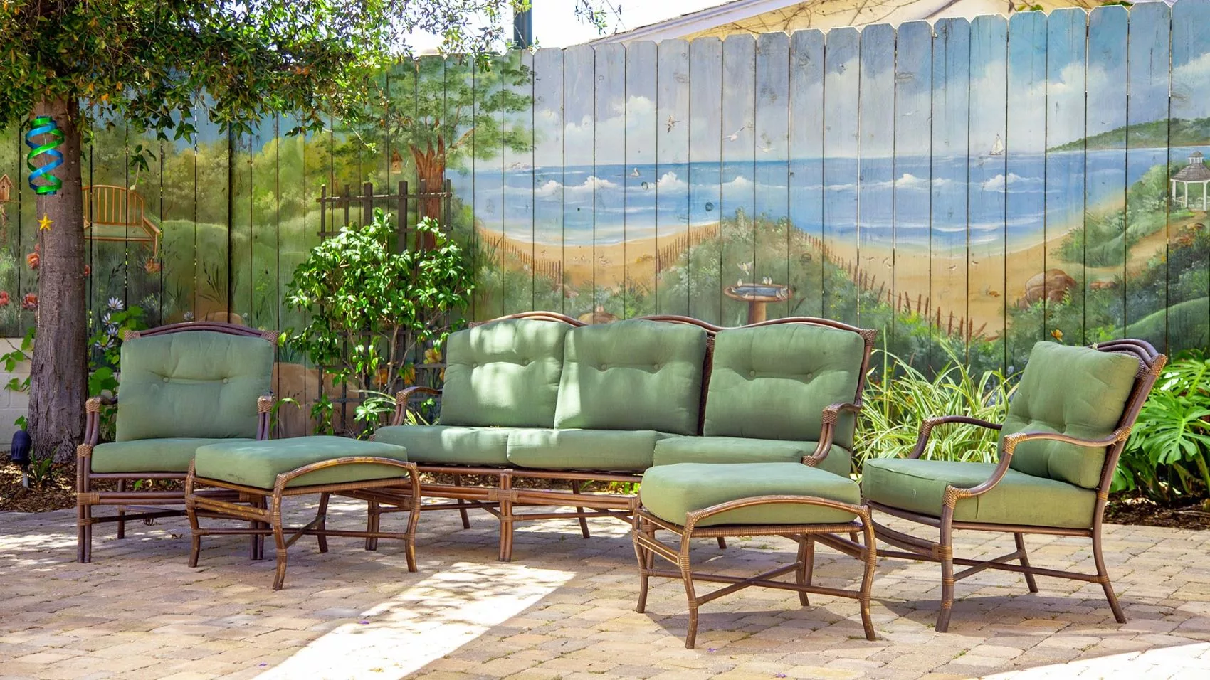 A cozy outdoor patio setting with green cushioned furniture and a beach-themed mural on a wooden fence.