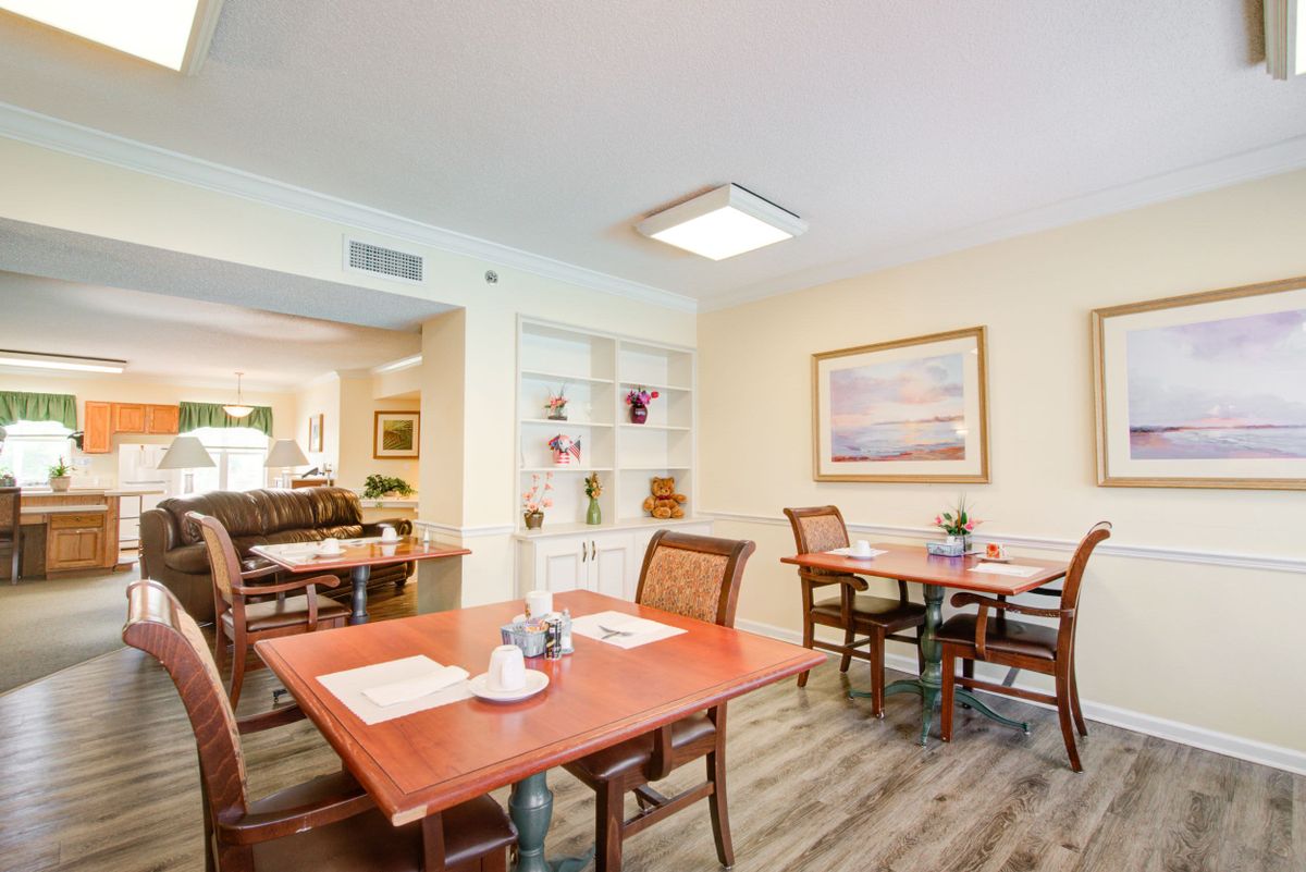 A well-lit dining room with neatly arranged tables and chairs, adorned with artwork on the walls.