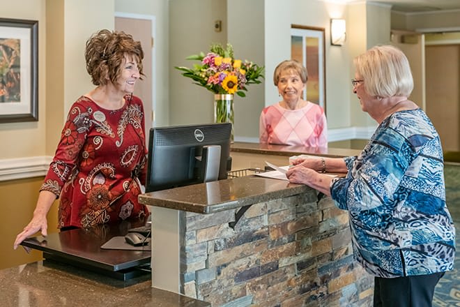 A receptionist and visitors interacting at a front desk in an office setting.