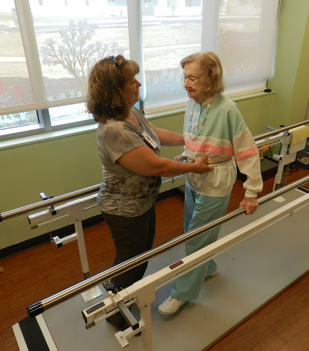 A healthcare professional assists an elderly patient during a physical therapy session.