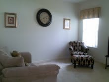 A cozy living room with a sofa, patterned chair, wall clock, and window.