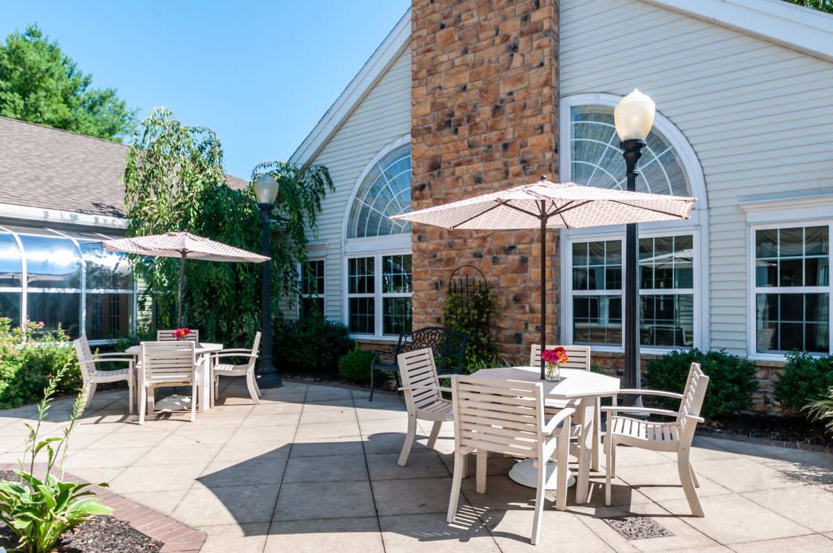 A sunny outdoor patio area with tables, chairs, and umbrellas adjacent to a building.