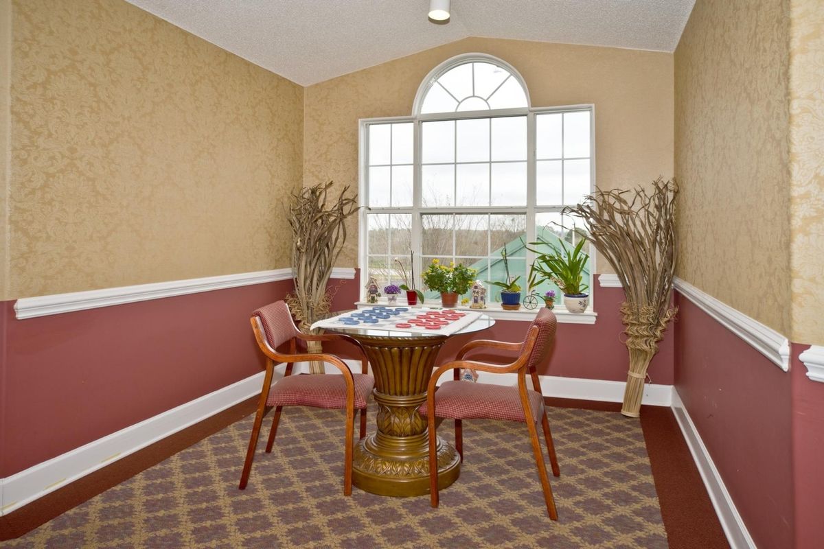 A cozy living room interior with a small table and chairs by the window, adorned with plants and decorative elements.