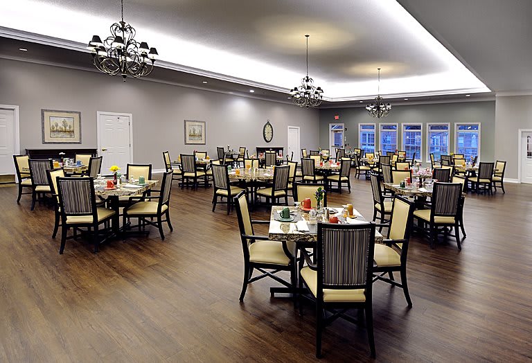 An elegant dining room with neatly arranged tables and chairs, lit by chandeliers.