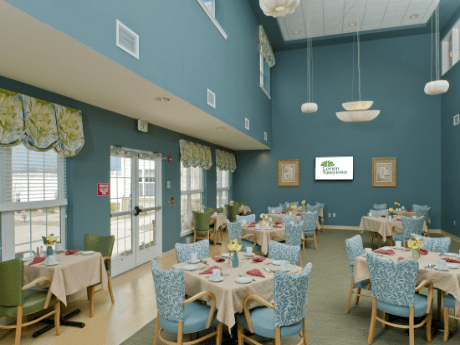 A spacious dining room with blue walls, set with tables and chairs, featuring elegant lighting fixtures.