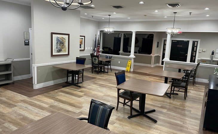 A spacious, empty room with tables and chairs, featuring flags, chandeliers, and artwork on the walls.