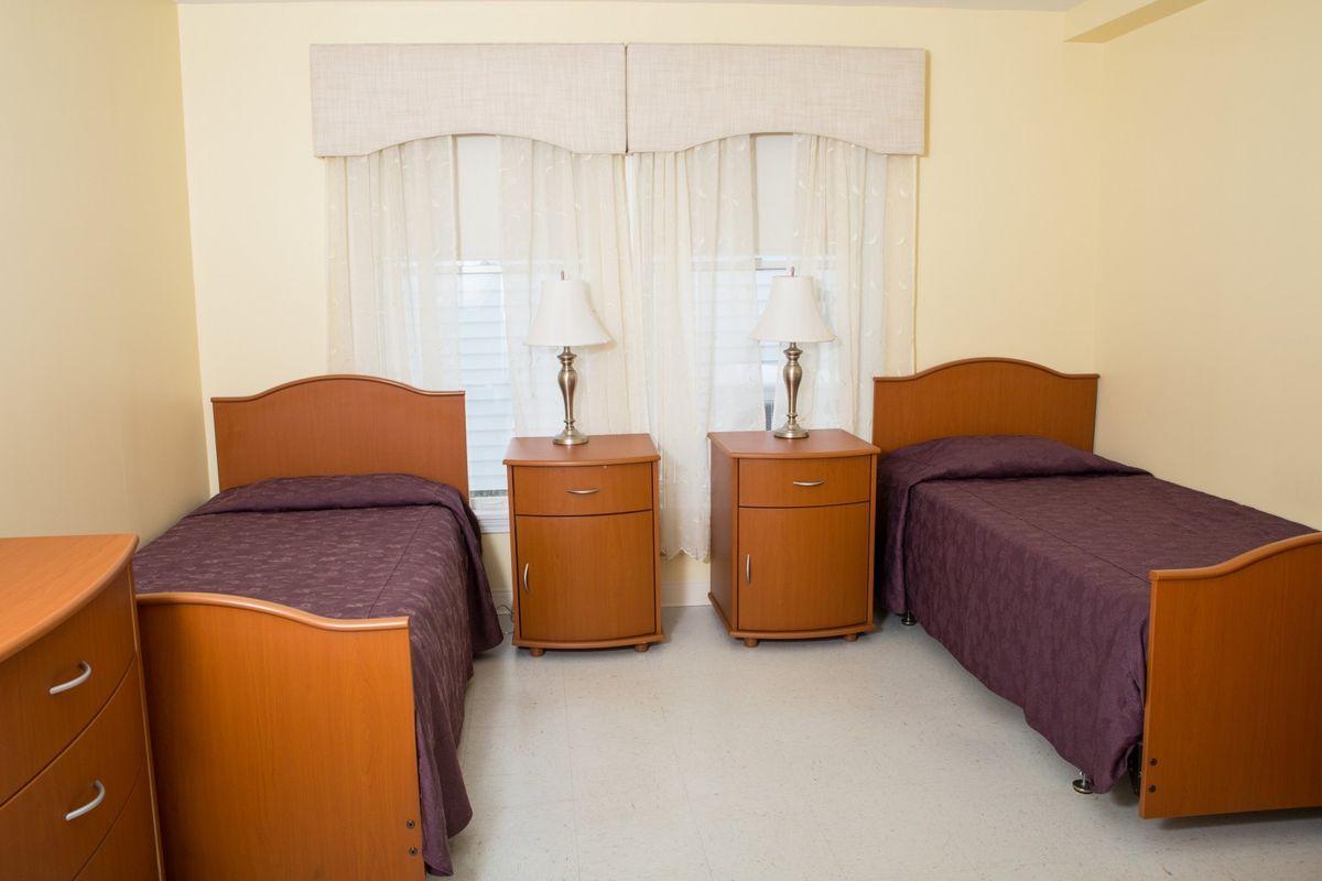 A cozy bedroom with two twin beds, each accompanied by a nightstand and lamp, set against a large window with curtains.