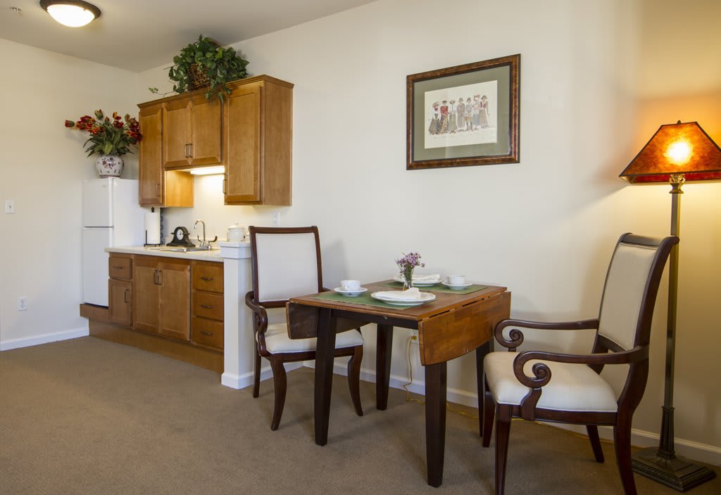 A cozy dining area with a small table and two chairs next to a kitchenette, adorned with wall art and subtle decor.