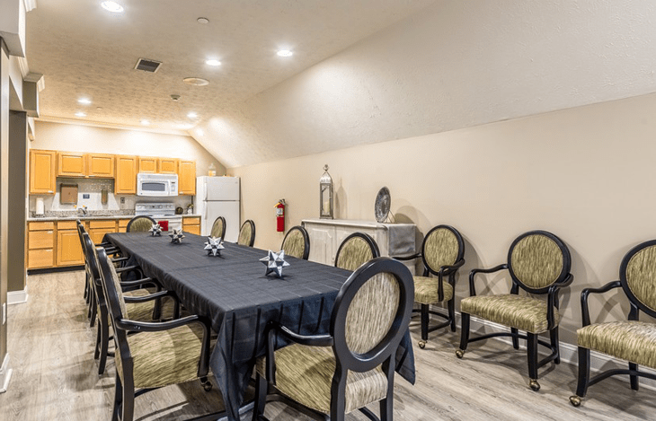 A well-equipped meeting room with a long table and chairs, adjacent to a kitchen area.