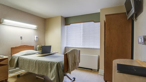 A well-lit hospital room featuring a single bed, a window with blinds, and minimalist decor.