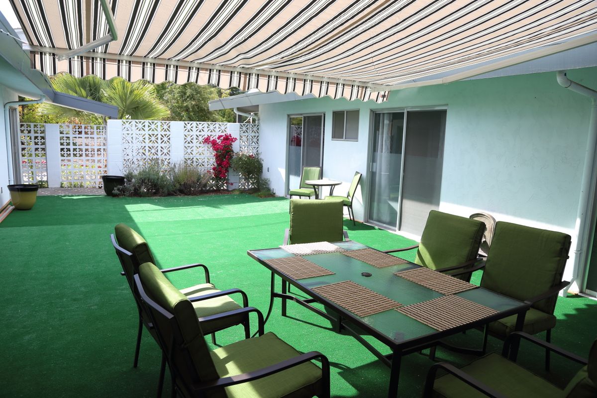 A covered patio area with green carpet, featuring outdoor seating and a table.