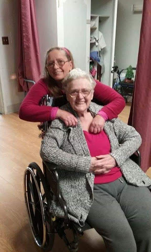 A joyful moment shared between two women, one in a wheelchair and the other offering loving support.