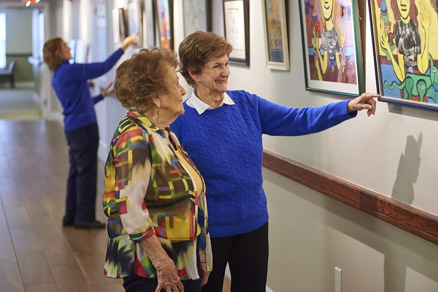 Two elderly women admire paintings in an art gallery, engaging in a lively conversation.