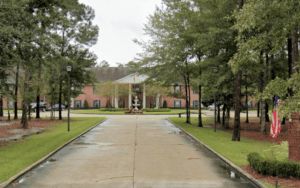 A view of a building surrounded by trees with a paved driveway leading up to it.
