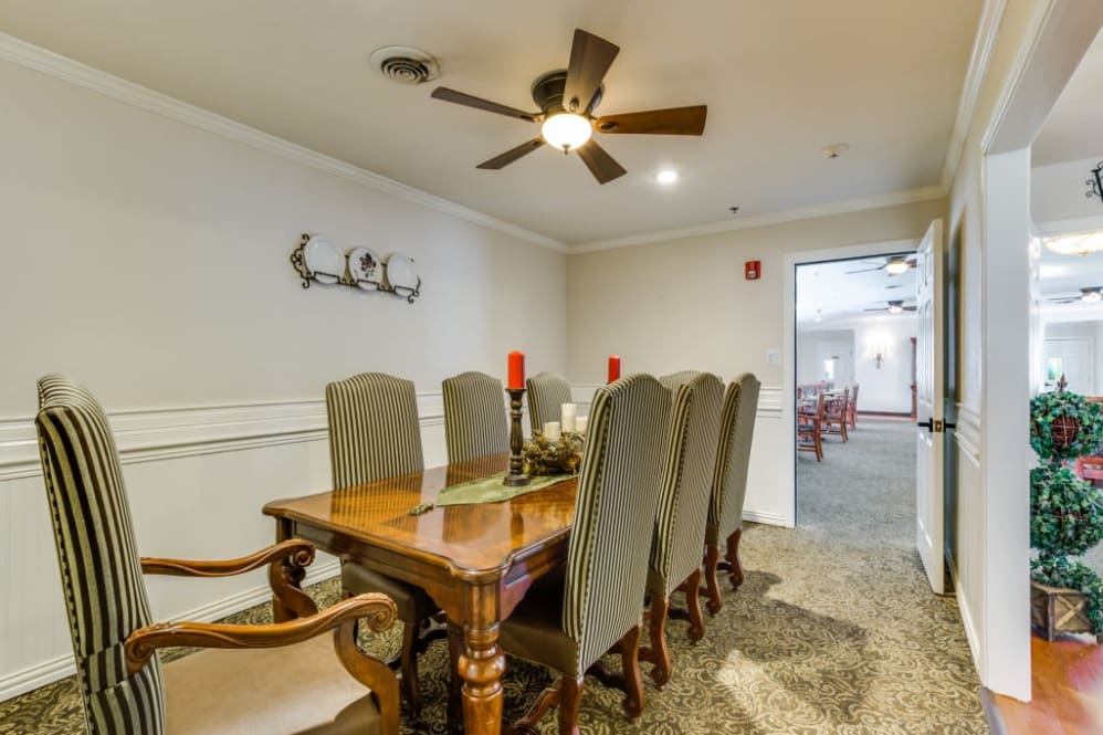 A well-furnished dining room with a wooden table, cushioned chairs, and a ceiling fan.