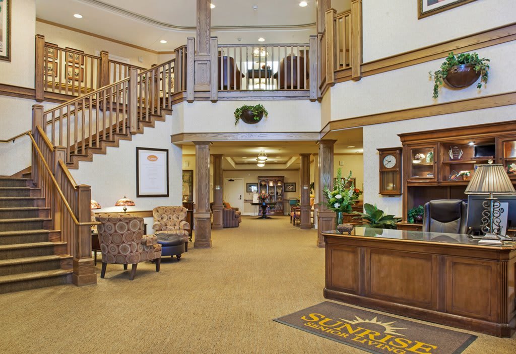 A warmly decorated hotel lobby featuring a reception desk, comfortable seating, and a staircase leading to an upper level.