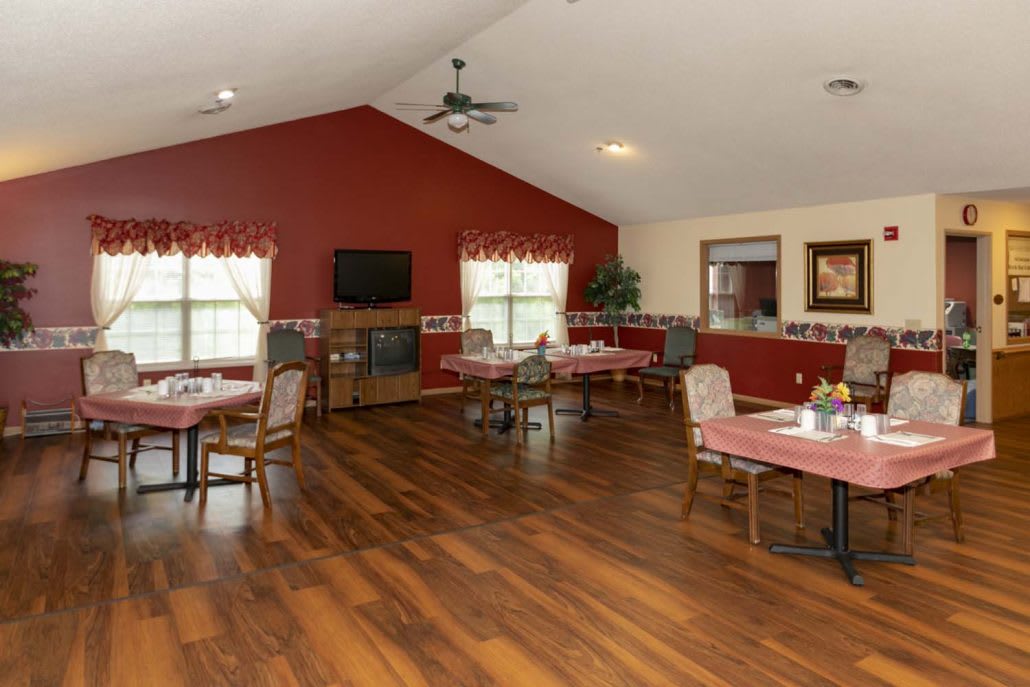 A cozy dining area with wooden floors and red accent walls, featuring several tables and chairs.