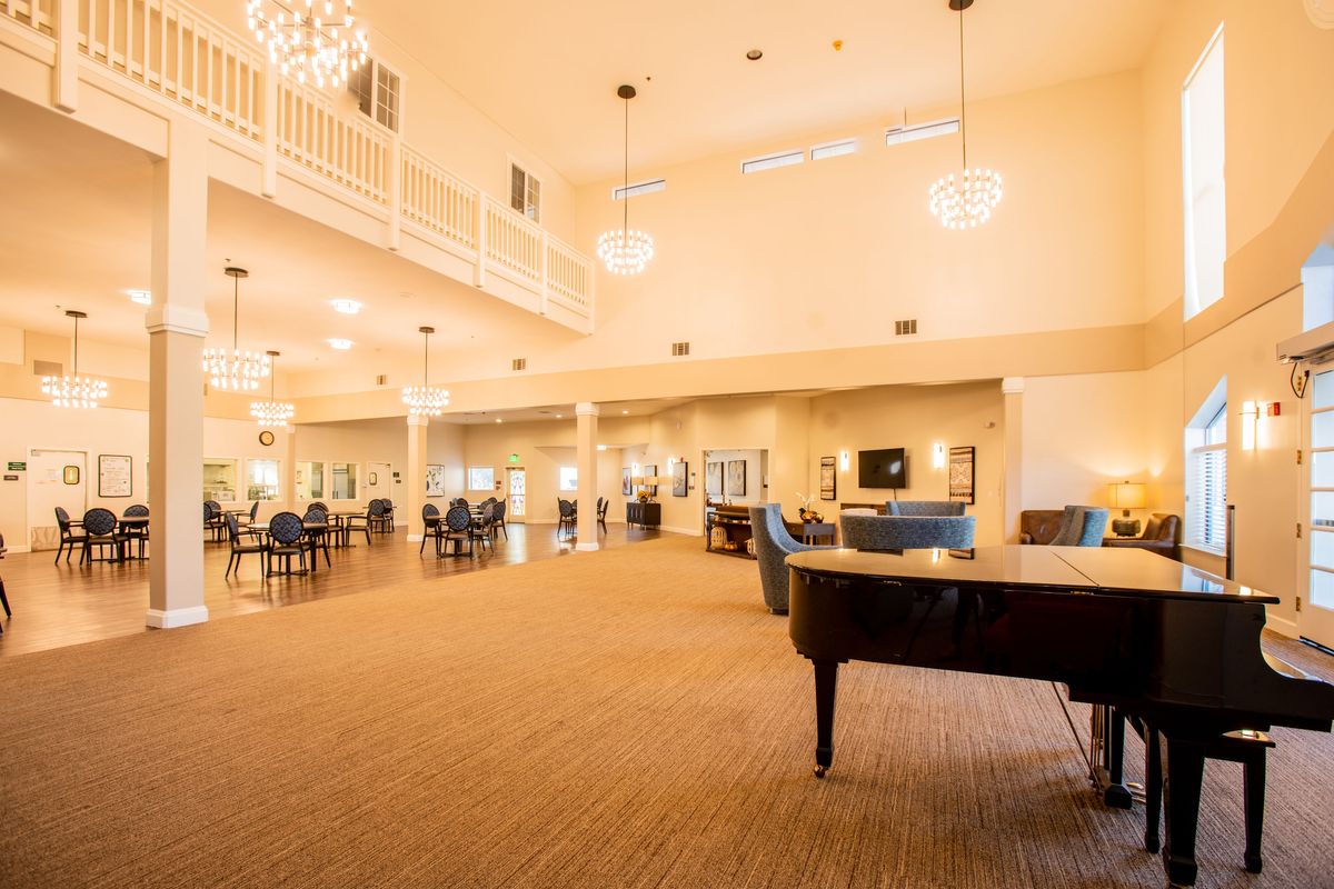 A spacious and elegant lounge area featuring a grand piano, chandeliers, and comfortable seating.