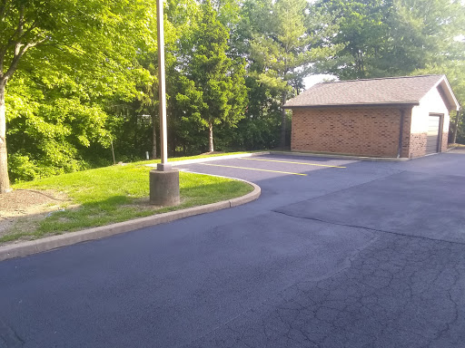 A serene parking lot surrounded by lush greenery, featuring a brick building and a lamp post.