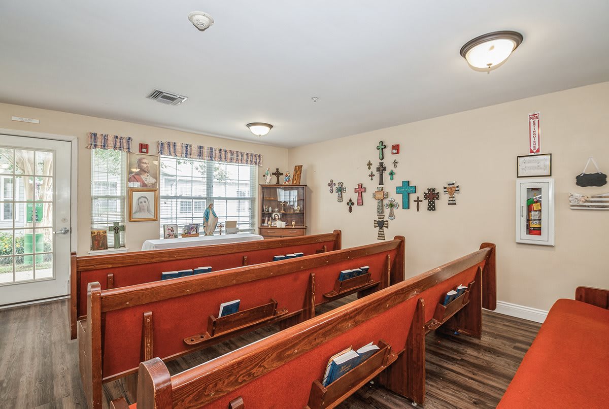 A small chapel interior featuring wooden pews and a wall adorned with various crosses.