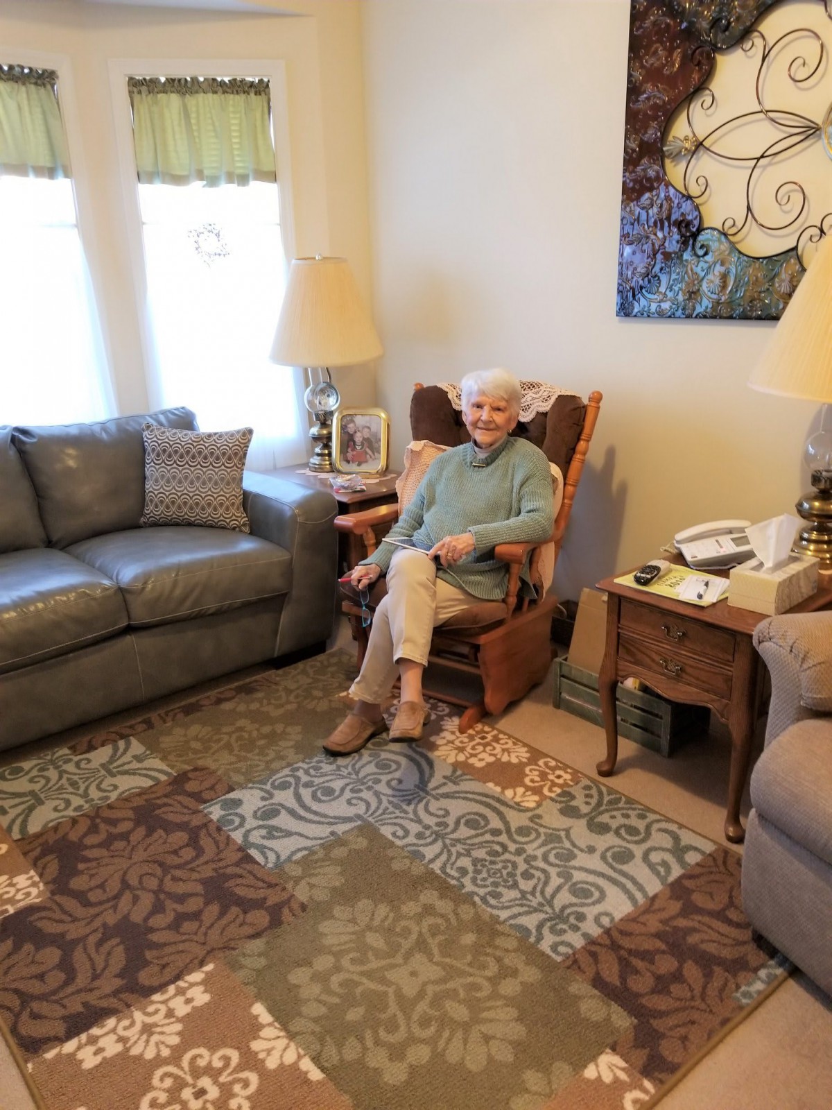 A woman sits comfortably in a living room on a rocking chair surrounded by cozy furnishings.