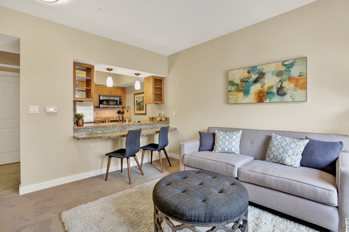 A modern living room with an open layout connected to the kitchen, featuring a comfortable sofa, stylish chairs, and abstract artwork on the wall.