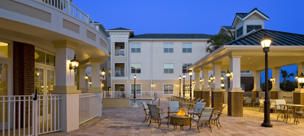 A hotel courtyard with outdoor seating and a fire pit, illuminated in the evening.