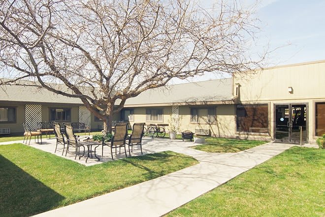 A peaceful courtyard featuring a tree, patio furniture, and a walkway.