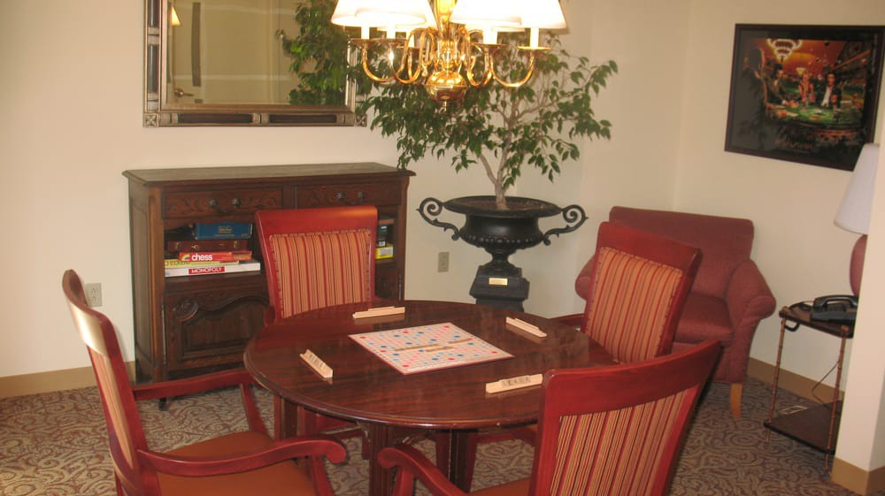 A cozy room with a table set for a board game, surrounded by chairs and illuminated by an overhead lamp.