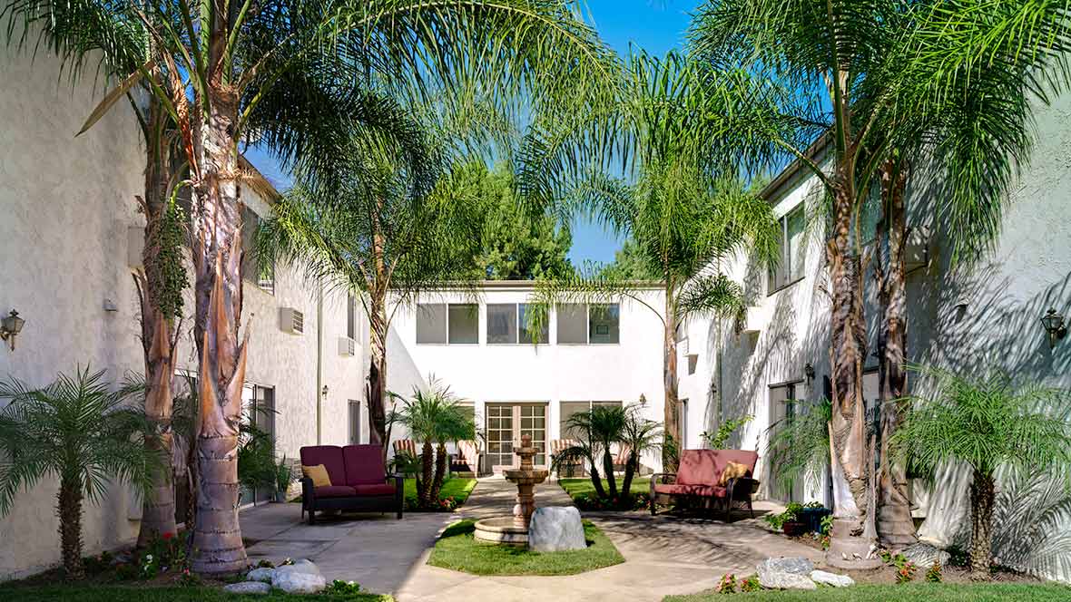 A sunny courtyard with palm trees and a central fountain surrounded by comfortable outdoor seating.