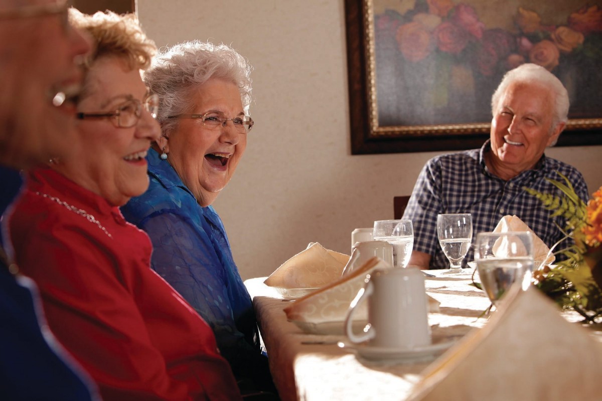 A group of seniors enjoying a joyful moment together at a dining table.