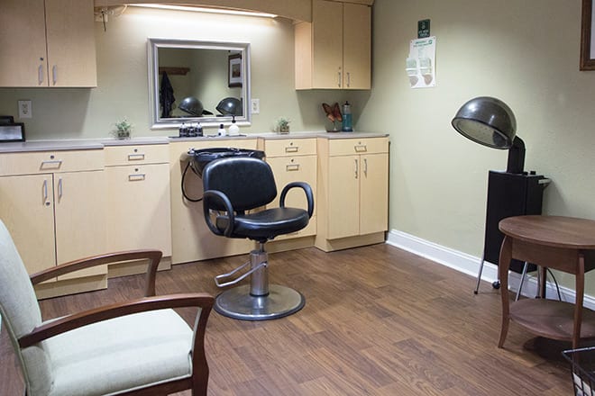 An empty salon with a styling chair, mirror, and hair dryer.