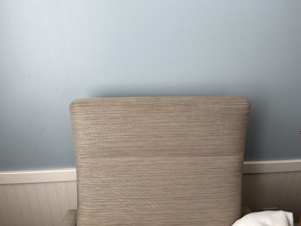 A beige upholstered chair against a light blue wall.
