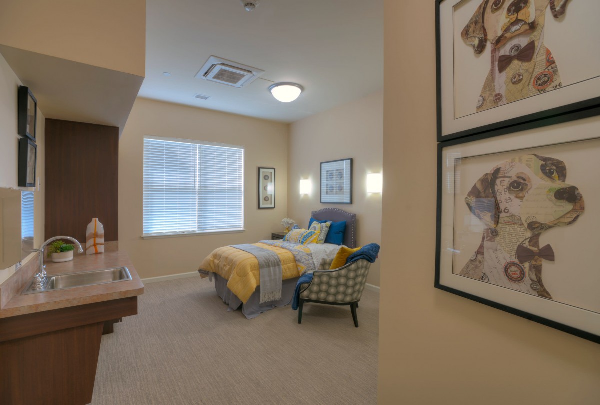 A cozy bedroom with a neatly made bed, artwork on the walls, and a comfortable chair.