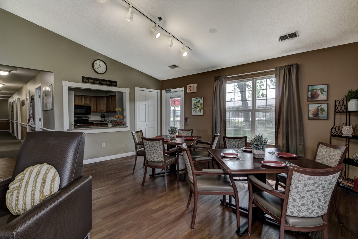 A cozy dining area with wooden tables and chairs, featuring large windows and elegant curtains.
