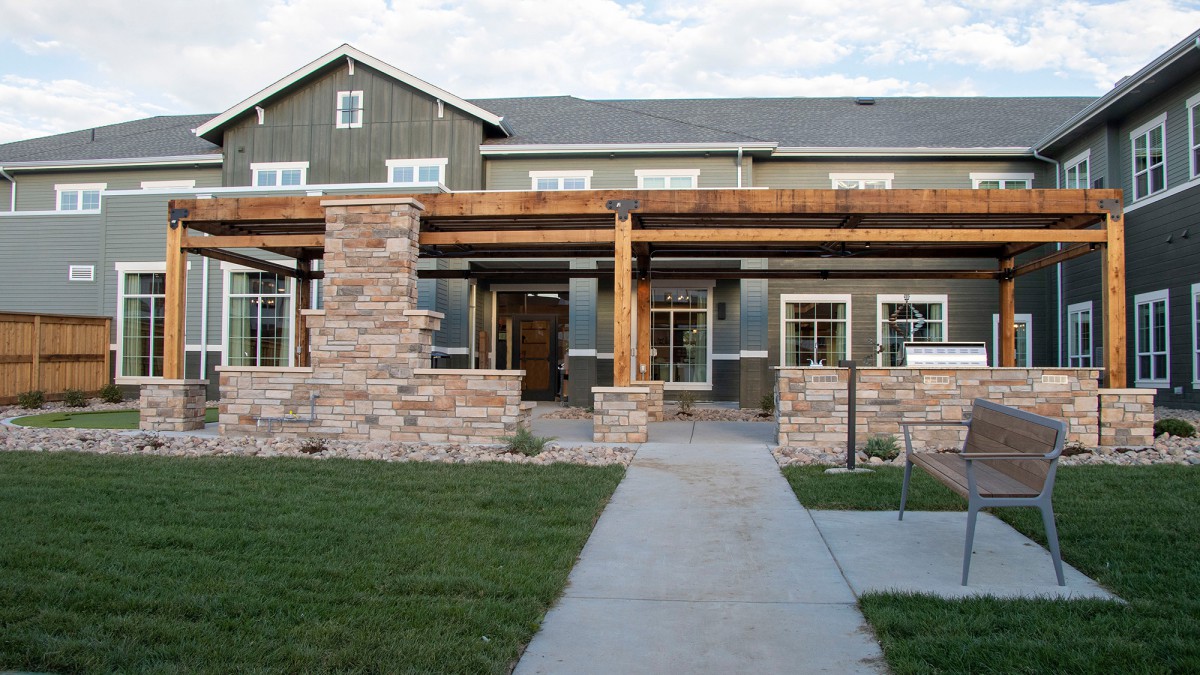 A modern two-story house with a stone facade and a wooden pergola at the entrance.