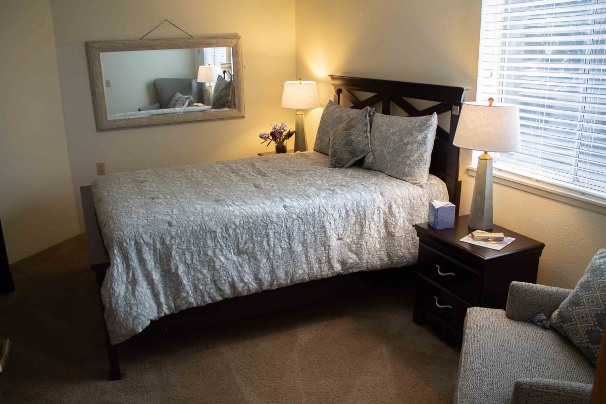 A cozy bedroom featuring a neatly made bed with patterned bedding, flanked by two elegant lamps on nightstands and a large mirror above the headboard.