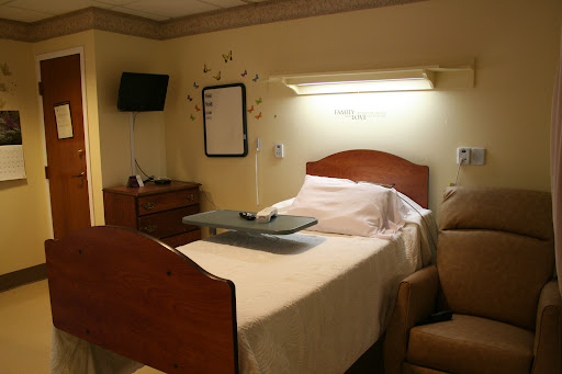 A hospital room featuring a bed with a tray table, a TV mounted on the wall, and a comfortable chair.