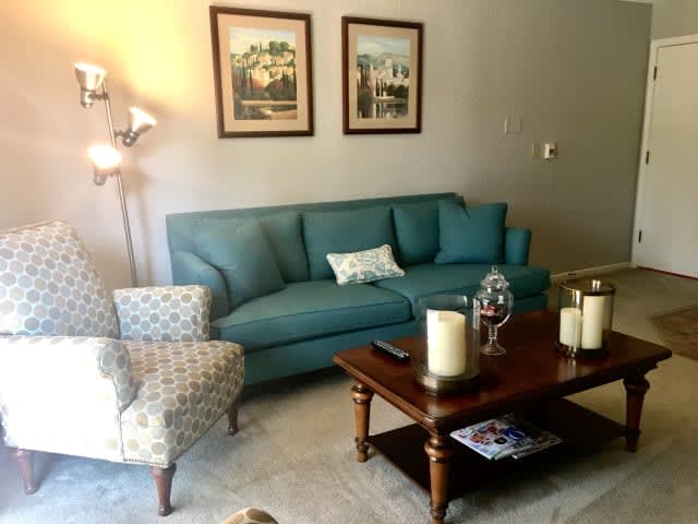 Cozy living room with a teal sofa, patterned armchair, and a wooden coffee table adorned with candles.