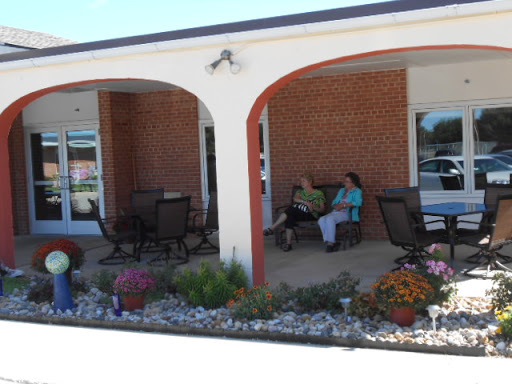 A serene outdoor seating area in front of a brick building, featuring women enjoying a leisurely moment amidst colorful flowers.
