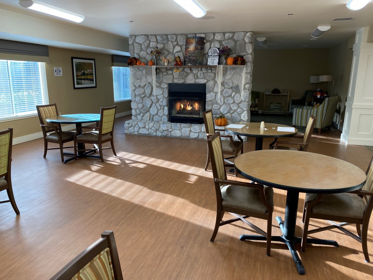 A cozy dining area with tables and chairs arranged around a fireplace.