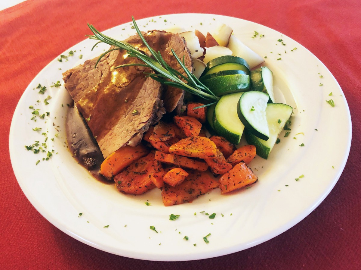A plate of roast beef with a side of sliced cucumbers, roasted carrots, and potatoes, garnished with herbs.