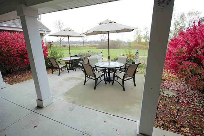 A cozy patio setup with outdoor tables, chairs, and umbrellas overlooking a garden.