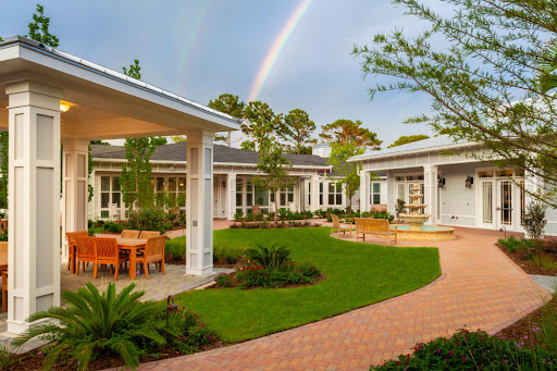 A serene outdoor space featuring contemporary architecture, lush greenery, and a vibrant rainbow in the background.