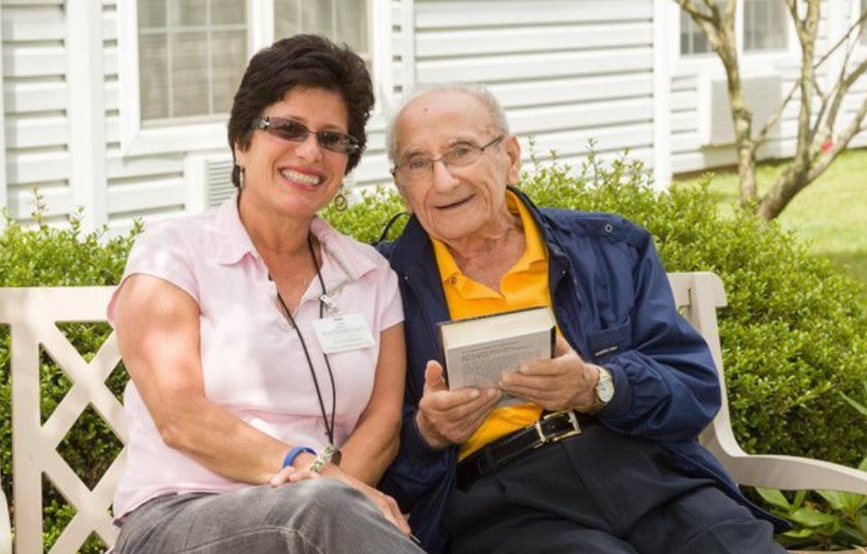 A happy elderly man and woman sitting together outdoors, with the man holding a book.
