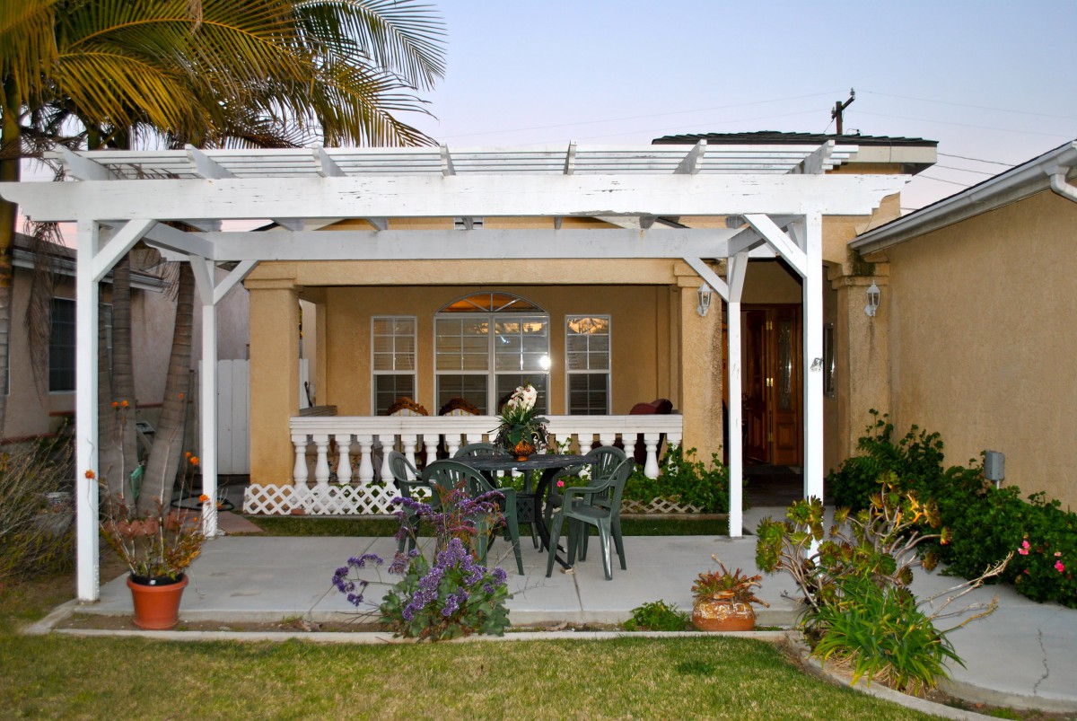 A cozy backyard patio with a pergola and outdoor seating surrounded by plants.